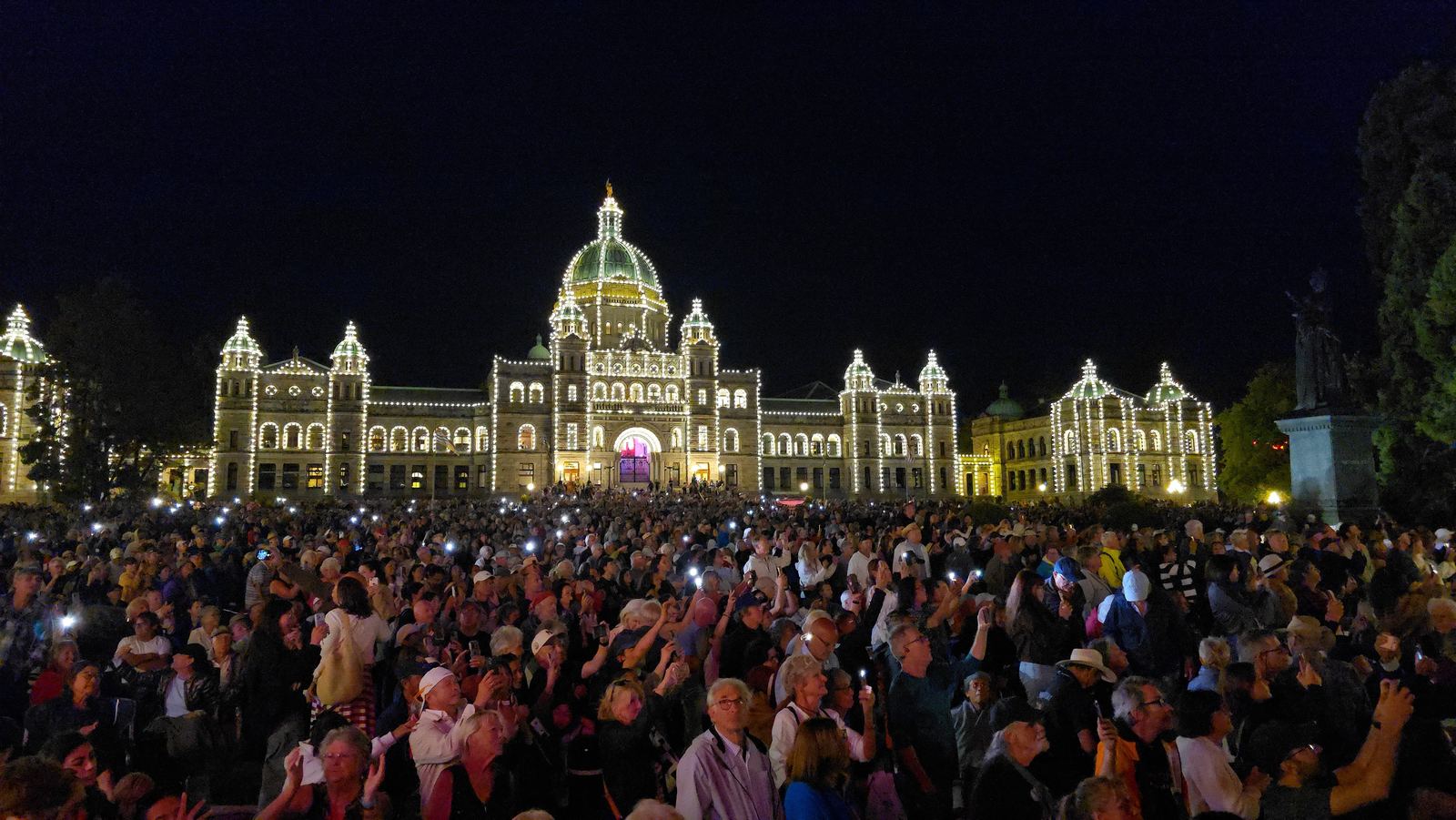 Large nighttime crowd at Victoria’s Inner Harbour and the illuminated British Columbia Parliament Buildings